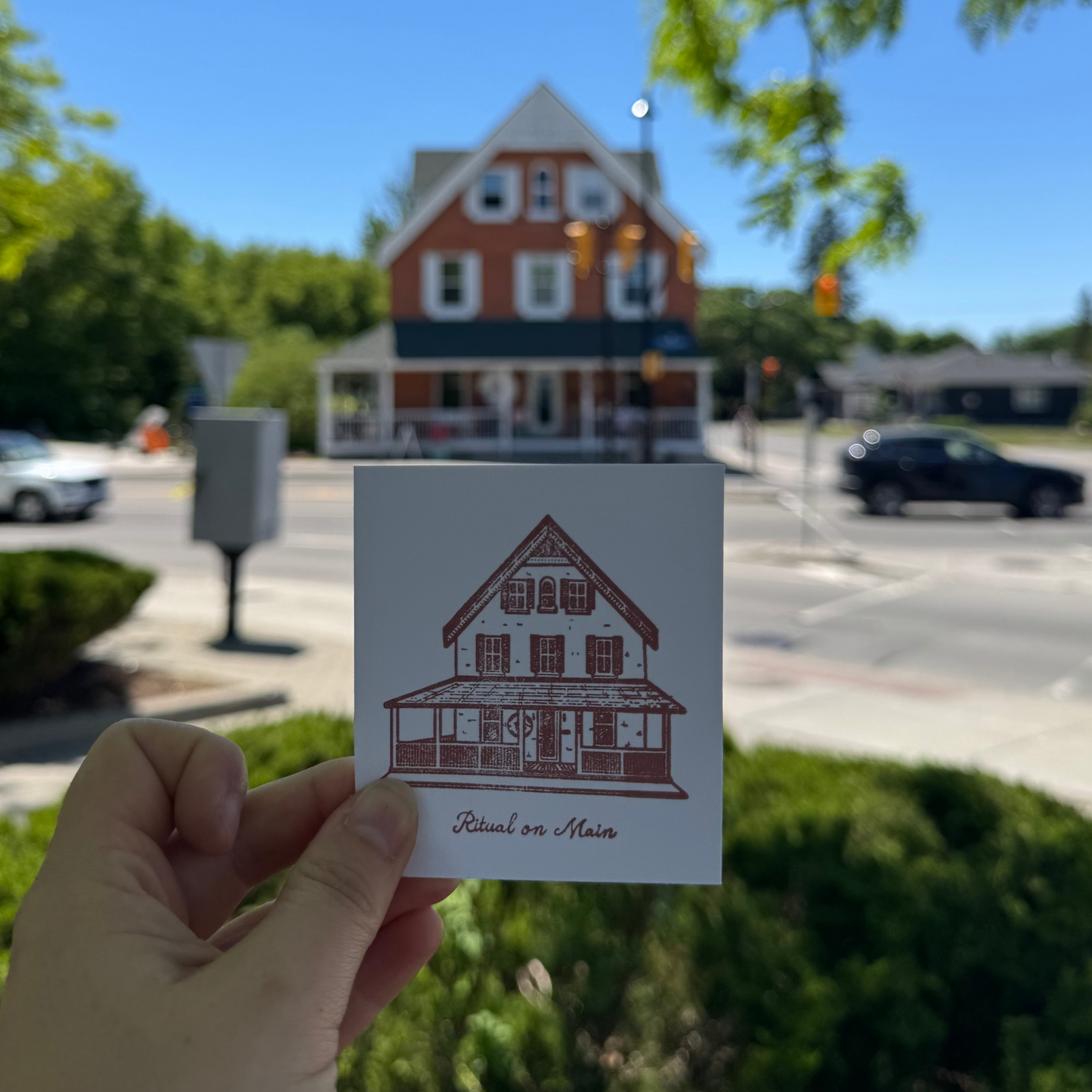 Hand holding a card with a house illustration in front of a street scene with a building.